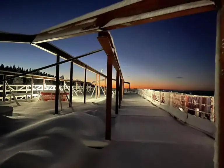 Utsikt over snødekt terrasse med byggestruktur under solnedgang, vinterlandskap.